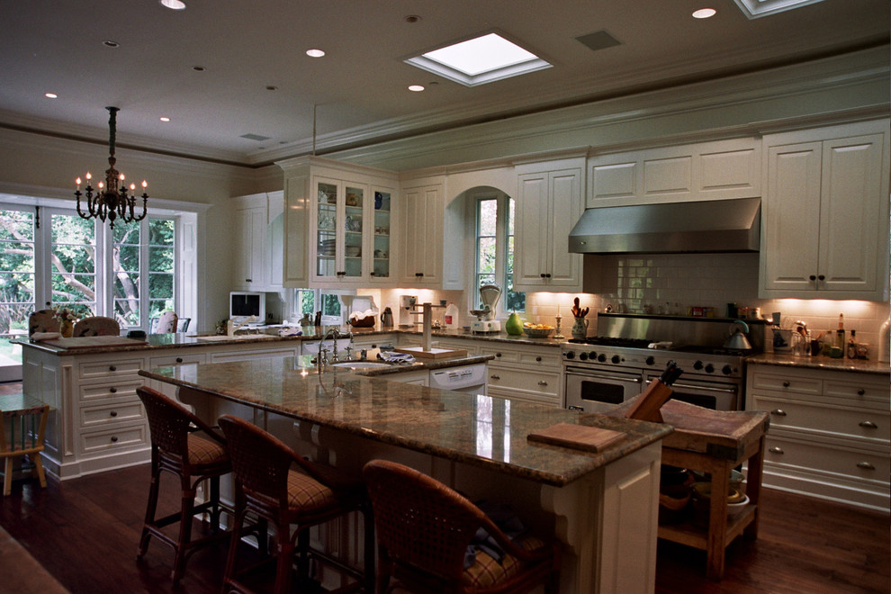 Eat-in kitchen - huge traditional u-shaped medium tone wood floor eat-in kitchen idea in Los Angeles with a drop-in sink, recessed-panel cabinets, white cabinets, granite countertops, white backsplash, subway tile backsplash, stainless steel appliances and an island