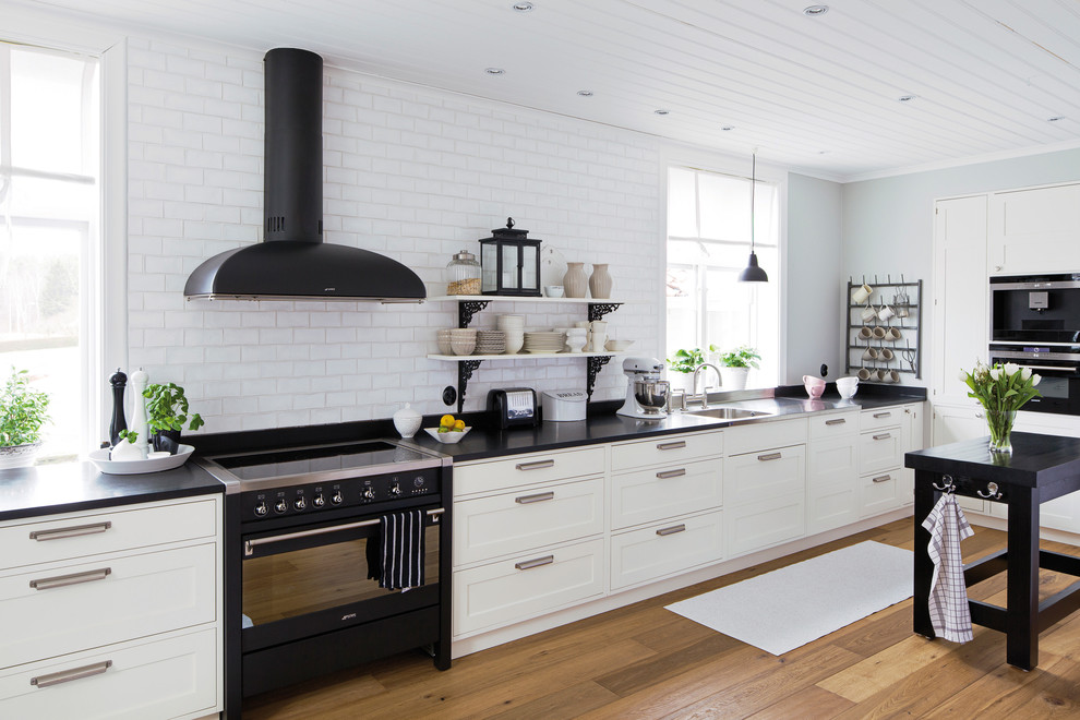 Große Skandinavische Küche mit Waschbecken, Schrankfronten im Shaker-Stil, schwarzen Elektrogeräten, braunem Holzboden und Kücheninsel in Göteborg