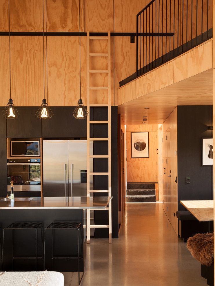 Kleine Moderne Wohnküche in L-Form mit Kücheninsel, schwarzen Schränken, Edelstahl-Arbeitsplatte, Küchengeräten aus Edelstahl und Betonboden in Dunedin