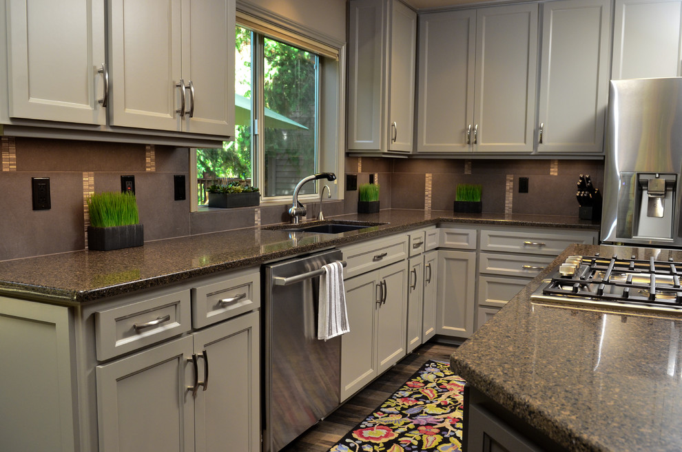 Klassisk inredning av ett kök och matrum, med en undermonterad diskho, luckor med infälld panel, grå skåp, granitbänkskiva, grått stänkskydd, rostfria vitvaror och en köksö