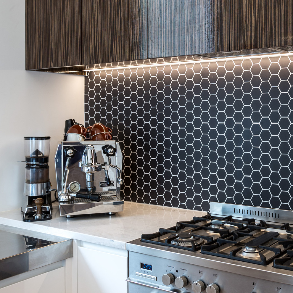 Moderne Küche mit flächenbündigen Schrankfronten, weißen Schränken, Mineralwerkstoff-Arbeitsplatte, Küchenrückwand in Schwarz und Küchengeräten aus Edelstahl in Auckland