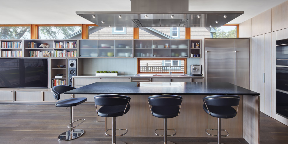 Offene Moderne Küche in L-Form mit flächenbündigen Schrankfronten, hellen Holzschränken, Küchengeräten aus Edelstahl, braunem Holzboden, Kücheninsel, braunem Boden und grauer Arbeitsplatte in Minneapolis