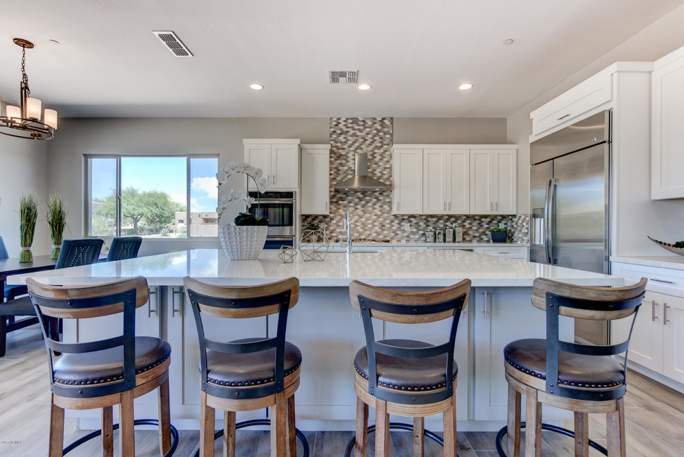 Open concept kitchen - mid-sized southwestern l-shaped light wood floor and brown floor open concept kitchen idea in Phoenix with an undermount sink, shaker cabinets, white cabinets, limestone countertops, multicolored backsplash, mosaic tile backsplash, stainless steel appliances and an island