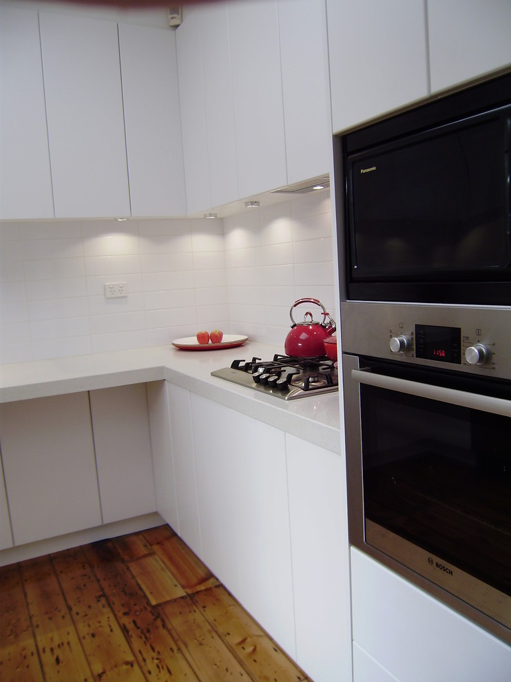 Bild på ett avskilt, litet funkis u-kök, med en dubbel diskho, släta luckor, vita skåp, bänkskiva i kvartsit, vitt stänkskydd, stänkskydd i keramik, rostfria vitvaror och mellanmörkt trägolv