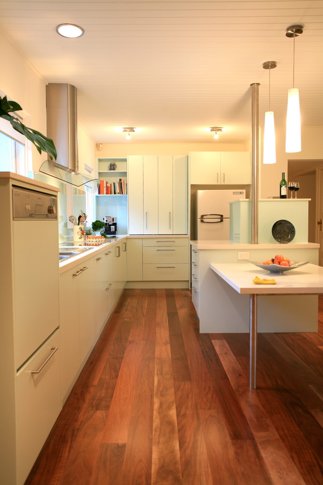 Example of a mid-sized minimalist l-shaped medium tone wood floor and brown floor enclosed kitchen design in Melbourne with a double-bowl sink, green cabinets, quartz countertops, green backsplash, glass sheet backsplash, stainless steel appliances and an island