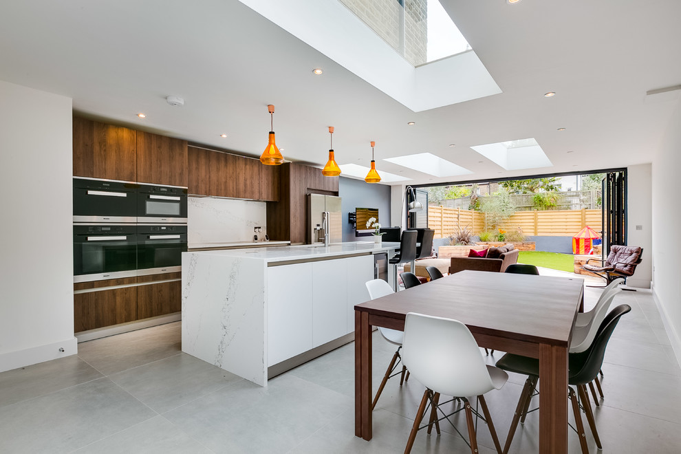 Photo of a contemporary galley open plan kitchen in London with flat-panel cabinets, dark wood cabinets, white splashback, black appliances and an island.