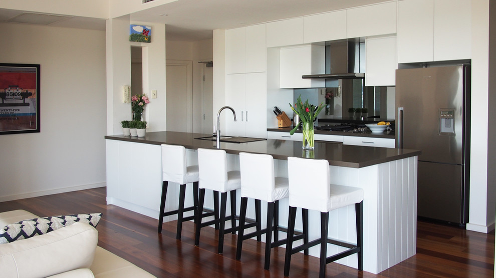 Inspiration for a medium sized contemporary galley open plan kitchen in Brisbane with a submerged sink, flat-panel cabinets, white cabinets, engineered stone countertops, mirror splashback, stainless steel appliances, dark hardwood flooring and an island.