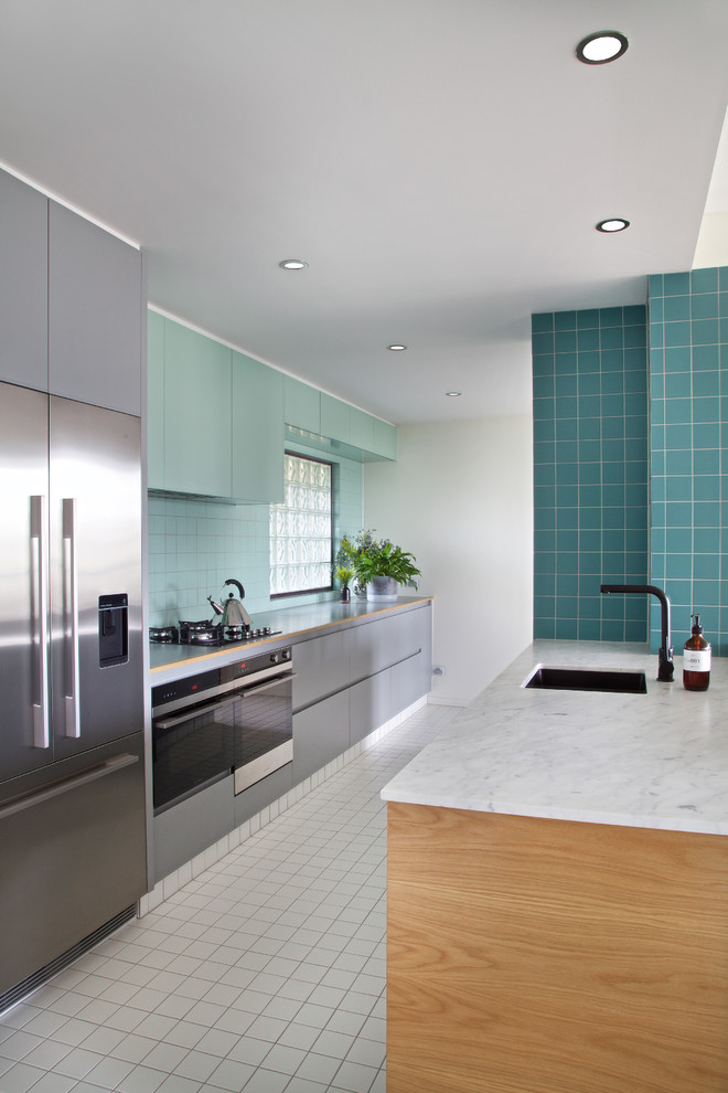 Diseño de cocina contemporánea con fregadero bajoencimera, armarios con paneles lisos, puertas de armario azules, salpicadero azul, electrodomésticos de acero inoxidable y península