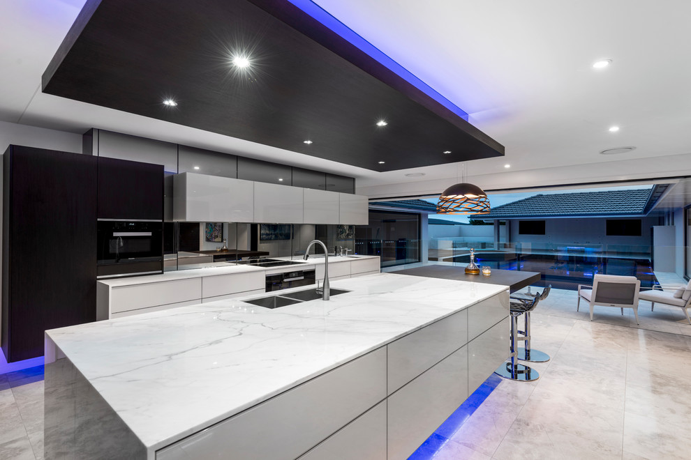 This is an example of an expansive contemporary galley open plan kitchen in Brisbane with a submerged sink, glass-front cabinets, beige cabinets, marble worktops, black splashback, mirror splashback, black appliances, travertine flooring, an island and beige floors.