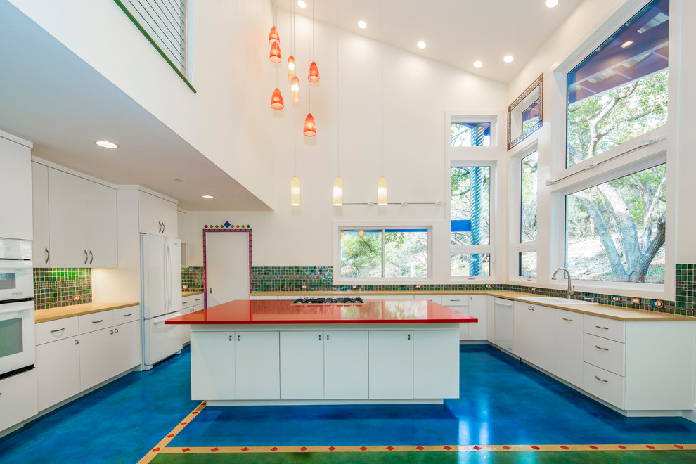 オースティンにある高級な中くらいなエクレクティックスタイルのおしゃれなキッチン (フラットパネル扉のキャビネット、白いキャビネット、マルチカラーのキッチンパネル、ガラスタイルのキッチンパネル、白い調理設備、コンクリートの床) の写真