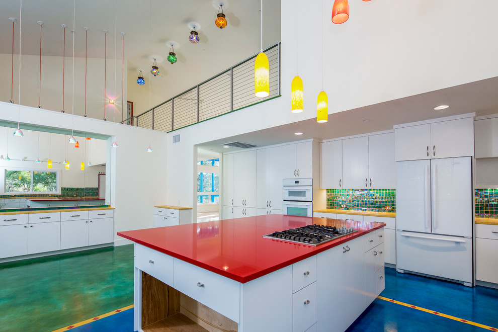 Medium sized eclectic u-shaped kitchen/diner in Austin with flat-panel cabinets, white cabinets, multi-coloured splashback, glass tiled splashback, white appliances, concrete flooring and an island.