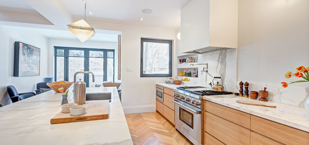 This is an example of a medium sized scandi single-wall kitchen/diner in Toronto with a submerged sink, flat-panel cabinets, light wood cabinets, marble worktops, white splashback, marble splashback, stainless steel appliances, light hardwood flooring, an island, beige floors and white worktops.