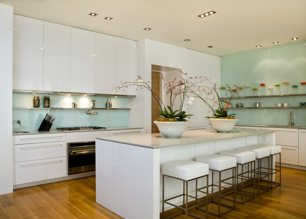 This is an example of a contemporary l-shaped kitchen in Toronto with flat-panel cabinets, white cabinets, blue splashback, glass sheet splashback and stainless steel appliances.