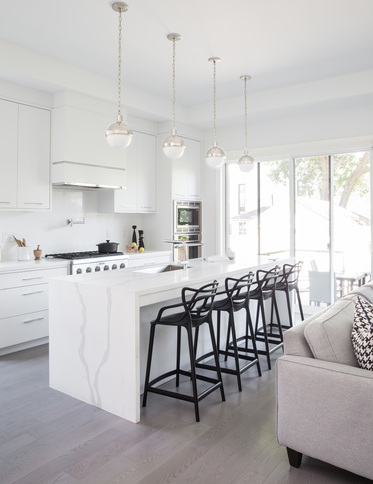 Large trendy l-shaped light wood floor and gray floor open concept kitchen photo in Toronto with an undermount sink, flat-panel cabinets, white cabinets, quartz countertops, white backsplash, stone slab backsplash, stainless steel appliances, an island and white countertops