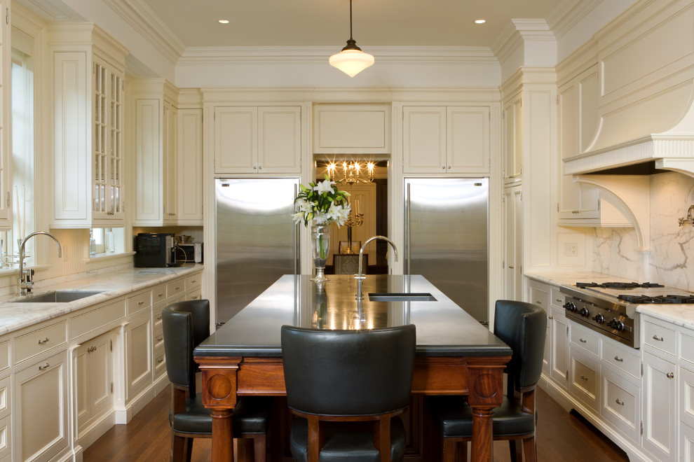 Example of a large classic galley dark wood floor enclosed kitchen design in Toronto with an undermount sink, shaker cabinets, white cabinets, white backsplash, stainless steel appliances, marble countertops, stone slab backsplash and an island