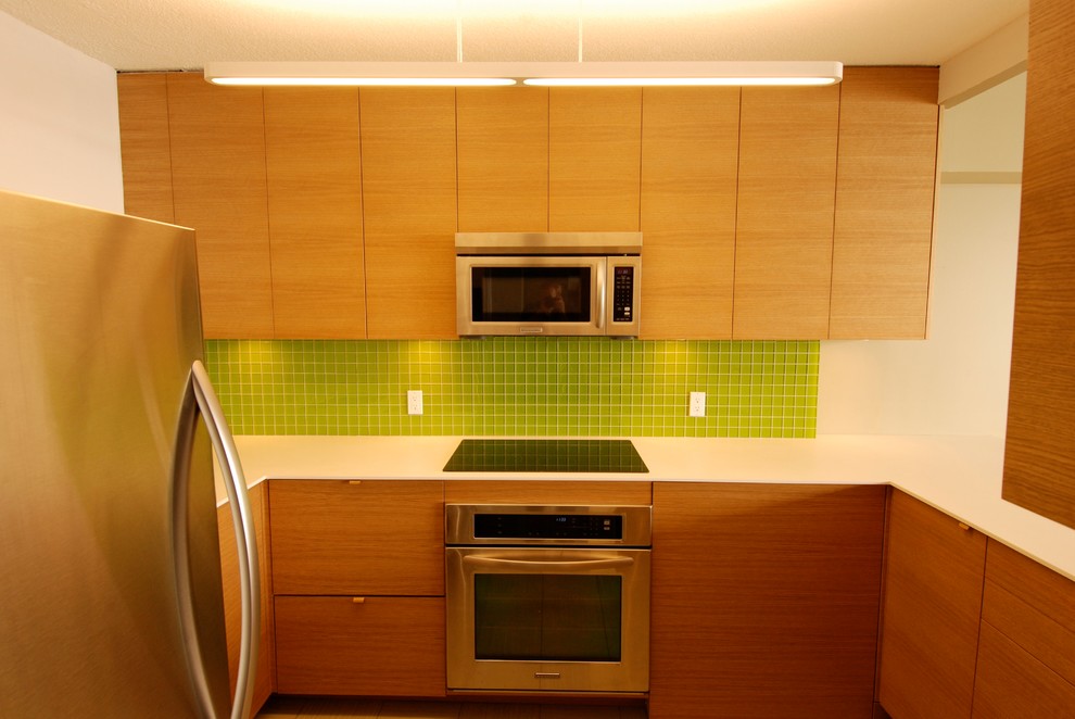 Стильный дизайн: п-образная кухня в современном стиле с обеденным столом, врезной мойкой, плоскими фасадами, светлыми деревянными фасадами, зеленым фартуком, фартуком из стеклянной плитки и техникой из нержавеющей стали - последний тренд