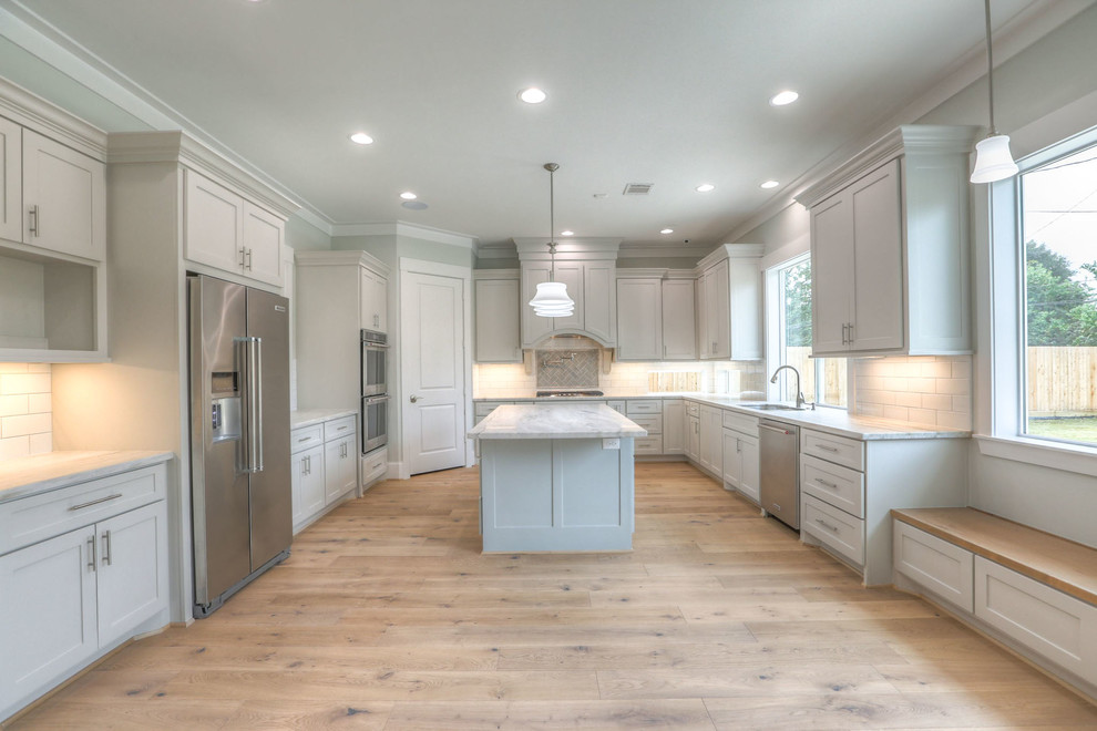 This is an example of a large traditional u-shaped enclosed kitchen in Houston with a double-bowl sink, shaker cabinets, grey cabinets, stainless steel worktops, white splashback, metro tiled splashback, stainless steel appliances, light hardwood flooring, an island and brown floors.