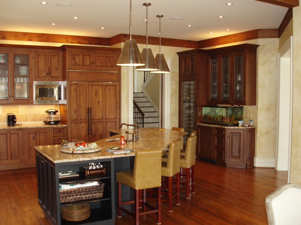 Medelhavsstil inredning av ett kök, med en rustik diskho, luckor med upphöjd panel, skåp i mellenmörkt trä, granitbänkskiva, beige stänkskydd, rostfria vitvaror, mörkt trägolv och en köksö