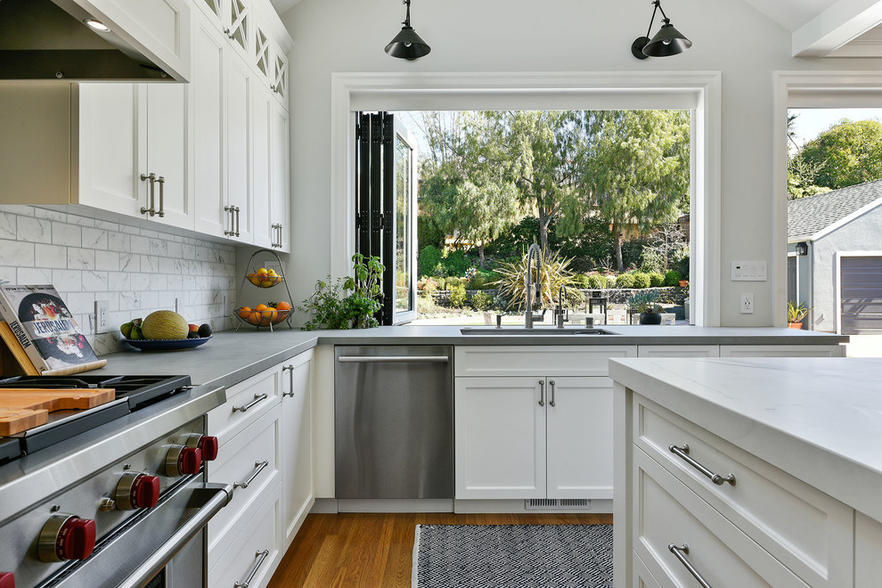 Idéer för ett avskilt, mellanstort 50 tals grå u-kök, med en undermonterad diskho, skåp i shakerstil, vita skåp, bänkskiva i betong, vitt stänkskydd, stänkskydd i marmor, rostfria vitvaror, mellanmörkt trägolv, en köksö och brunt golv