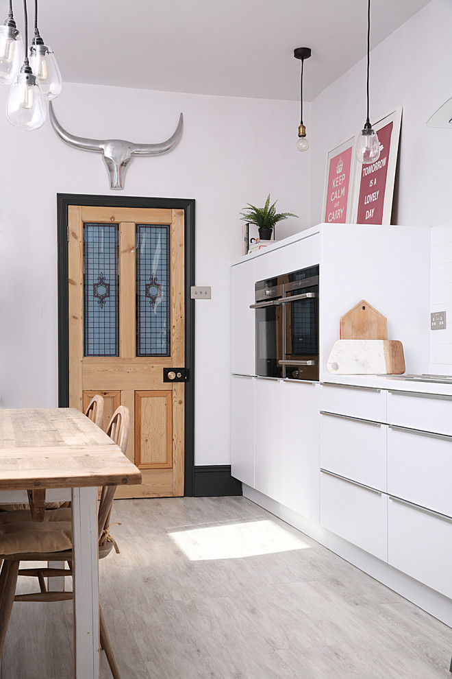 Foto på ett eklektiskt vit linjärt kök med öppen planlösning, med en undermonterad diskho, släta luckor, vita skåp, vitt stänkskydd, integrerade vitvaror, ljust trägolv och beiget golv
