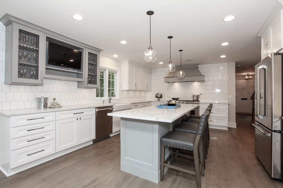 Inspiration for a large transitional l-shaped medium tone wood floor open concept kitchen remodel in Chicago with a farmhouse sink, recessed-panel cabinets, white cabinets, marble countertops, white backsplash, porcelain backsplash, stainless steel appliances and an island