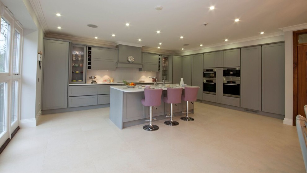 Große Moderne Küche in L-Form mit Schrankfronten im Shaker-Stil, grauen Schränken, Mineralwerkstoff-Arbeitsplatte, Küchenrückwand in Weiß und Halbinsel in Hertfordshire