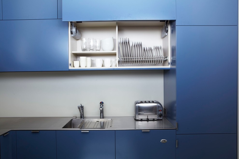 Kleine Moderne Wohnküche in U-Form mit integriertem Waschbecken, flächenbündigen Schrankfronten, blauen Schränken, Edelstahl-Arbeitsplatte, Küchenrückwand in Weiß, Glasrückwand, Küchengeräten aus Edelstahl und Porzellan-Bodenfliesen in Sydney