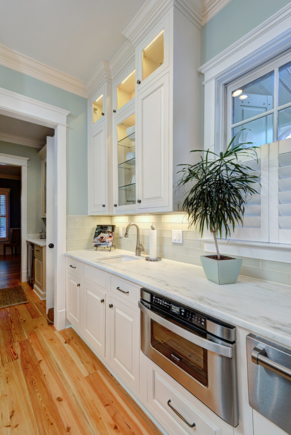 Example of a large trendy l-shaped light wood floor and beige floor eat-in kitchen design in Charleston with an island, a farmhouse sink, raised-panel cabinets, white cabinets, quartzite countertops, white backsplash, glass tile backsplash and stainless steel appliances