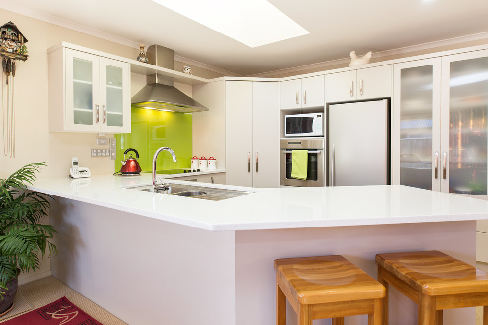 Mittelgroße Stilmix Wohnküche in U-Form mit Unterbauwaschbecken, flächenbündigen Schrankfronten, Küchenrückwand in Grün, Glasrückwand, Küchengeräten aus Edelstahl und Halbinsel in Christchurch