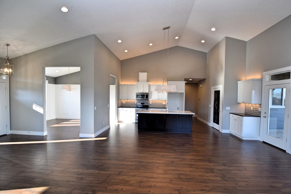 Inspiration for a large transitional l-shaped dark wood floor and brown floor open concept kitchen remodel in Portland with an undermount sink, shaker cabinets, white cabinets, quartz countertops, gray backsplash, subway tile backsplash, stainless steel appliances and an island