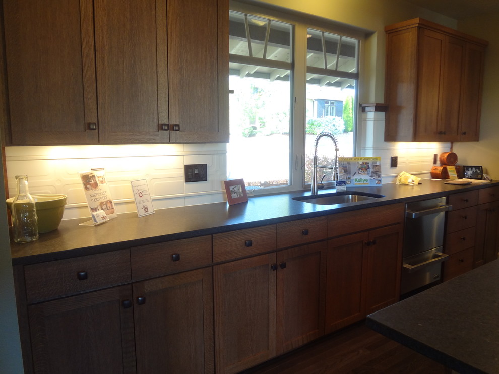 Example of a mid-sized classic galley dark wood floor eat-in kitchen design in Portland with an undermount sink, shaker cabinets, medium tone wood cabinets, laminate countertops, white backsplash, ceramic backsplash, stainless steel appliances and an island