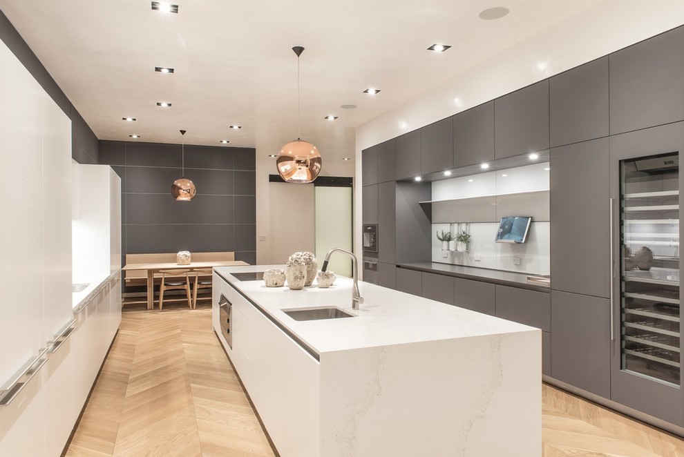 This is an example of a contemporary galley kitchen in Los Angeles with a submerged sink, flat-panel cabinets, grey cabinets, white splashback, light hardwood flooring and an island.