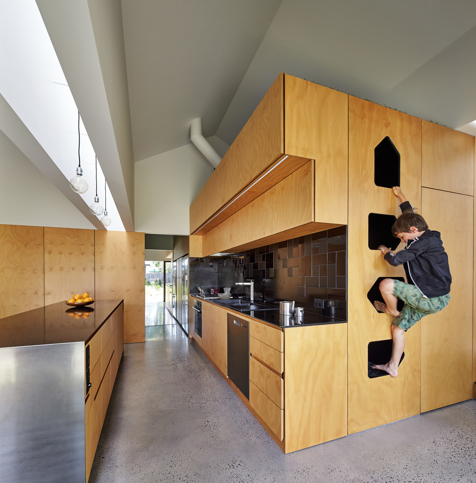Zweizeilige Moderne Küche mit flächenbündigen Schrankfronten, hellbraunen Holzschränken, Betonboden, Kücheninsel und Küchenrückwand in Schwarz in Melbourne