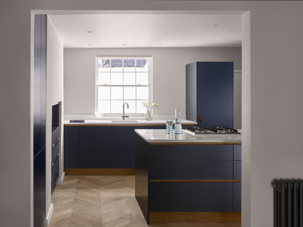 Inspiration for a contemporary l-shaped kitchen in London with a submerged sink, flat-panel cabinets, blue cabinets, integrated appliances, light hardwood flooring, an island, beige floors and white worktops.