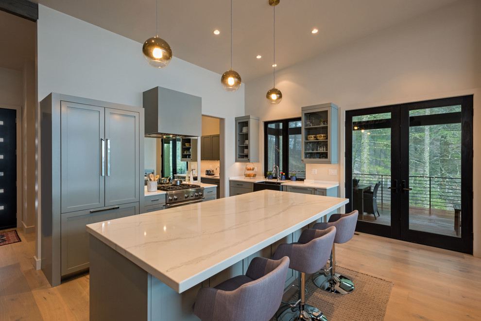 Example of a mid-sized minimalist l-shaped light wood floor and beige floor open concept kitchen design in Seattle with a farmhouse sink, recessed-panel cabinets, gray cabinets, quartzite countertops, white backsplash, mirror backsplash, paneled appliances and an island