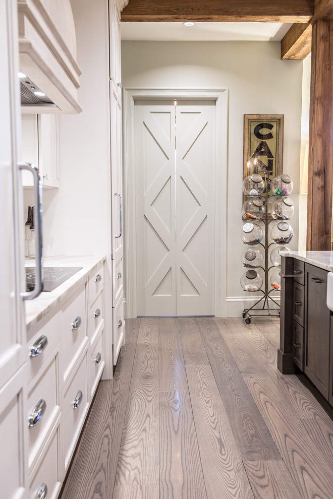 Example of a large mountain style single-wall medium tone wood floor eat-in kitchen design in St Louis with a farmhouse sink, shaker cabinets, white cabinets, marble countertops, white backsplash, subway tile backsplash, white appliances and an island