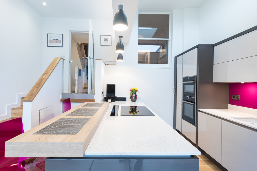 Bild på ett stort funkis kök och matrum, med en integrerad diskho, släta luckor, grå skåp, bänkskiva i kvartsit, rosa stänkskydd, stänkskydd i glaskakel, integrerade vitvaror, mellanmörkt trägolv och en köksö