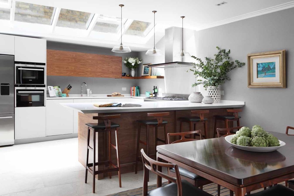 Inspiration for a traditional u-shaped kitchen in Other with flat-panel cabinets, white cabinets, grey splashback, glass sheet splashback, stainless steel appliances, a breakfast bar and white floors.