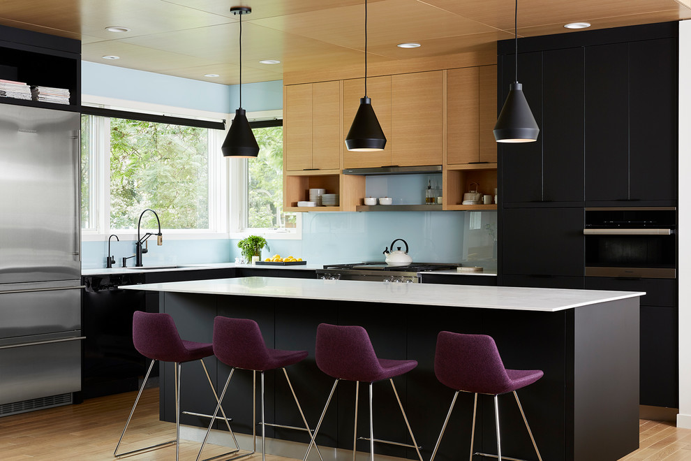 Modern inredning av ett kök och matrum, med svarta skåp, blått stänkskydd och rostfria vitvaror