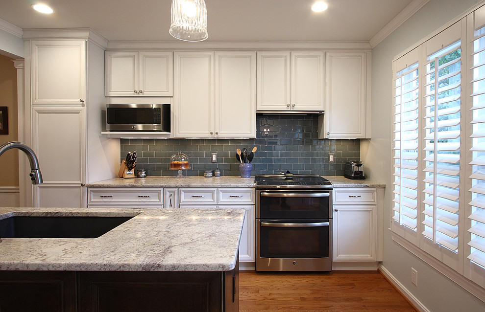 Exemple d'une cuisine chic avec des portes de placard blanches, un plan de travail en granite, une crédence bleue, un électroménager en acier inoxydable et îlot.