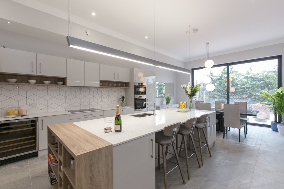 Zweizeilige Moderne Wohnküche mit Unterbauwaschbecken, flächenbündigen Schrankfronten, grauen Schränken, Küchenrückwand in Weiß, Küchengeräten aus Edelstahl, Kücheninsel, grauem Boden und weißer Arbeitsplatte in Belfast