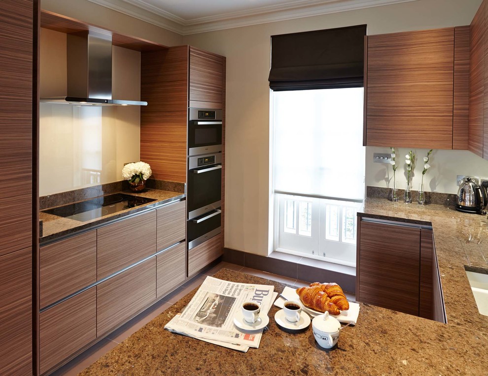 This is an example of a large traditional galley open plan kitchen in London with a submerged sink, flat-panel cabinets, medium wood cabinets, granite worktops, glass sheet splashback, stainless steel appliances, porcelain flooring and a breakfast bar.