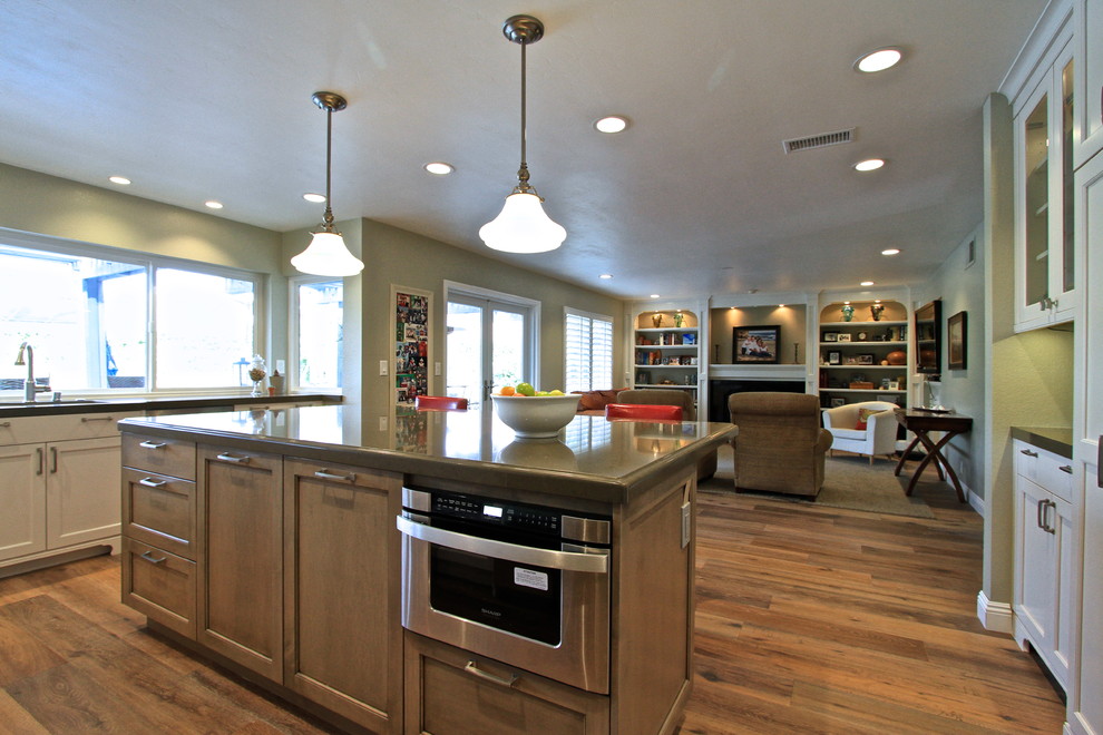 Klassisk inredning av ett mellanstort kök, med en undermonterad diskho, skåp i shakerstil, vita skåp, laminatbänkskiva, brunt stänkskydd, stänkskydd i stickkakel, rostfria vitvaror, mellanmörkt trägolv och en köksö