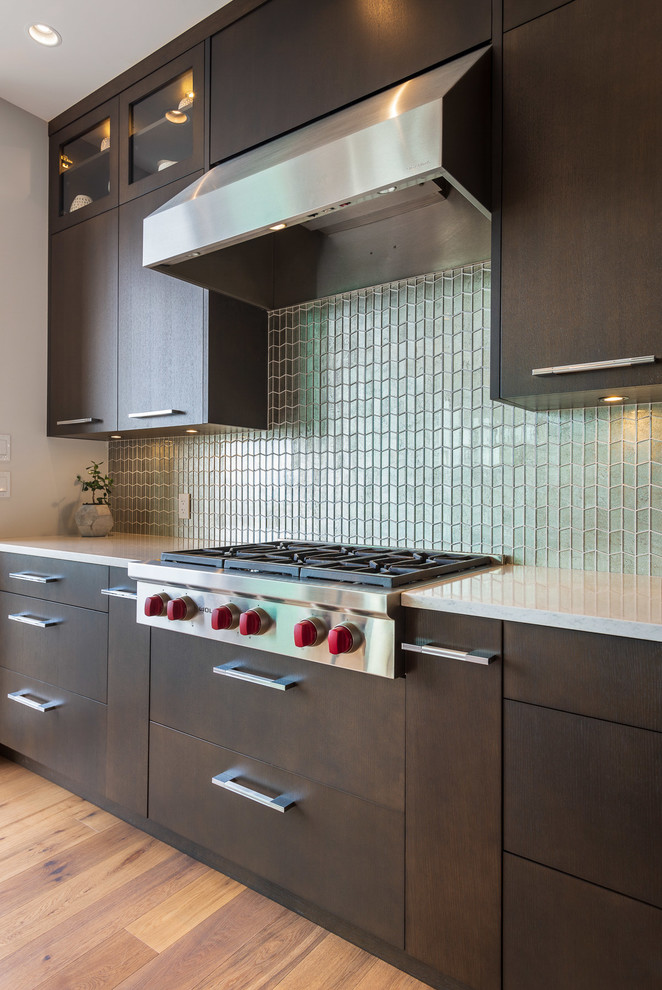 Large contemporary l-shaped kitchen/diner in Vancouver with a submerged sink, flat-panel cabinets, dark wood cabinets, quartz worktops, green splashback, glass tiled splashback, stainless steel appliances, light hardwood flooring, an island, brown floors and white worktops.
