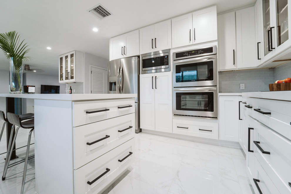 Large minimalist u-shaped ceramic tile and gray floor eat-in kitchen photo in Miami with an undermount sink, shaker cabinets, white cabinets, gray backsplash, glass tile backsplash, stainless steel appliances, an island and white countertops