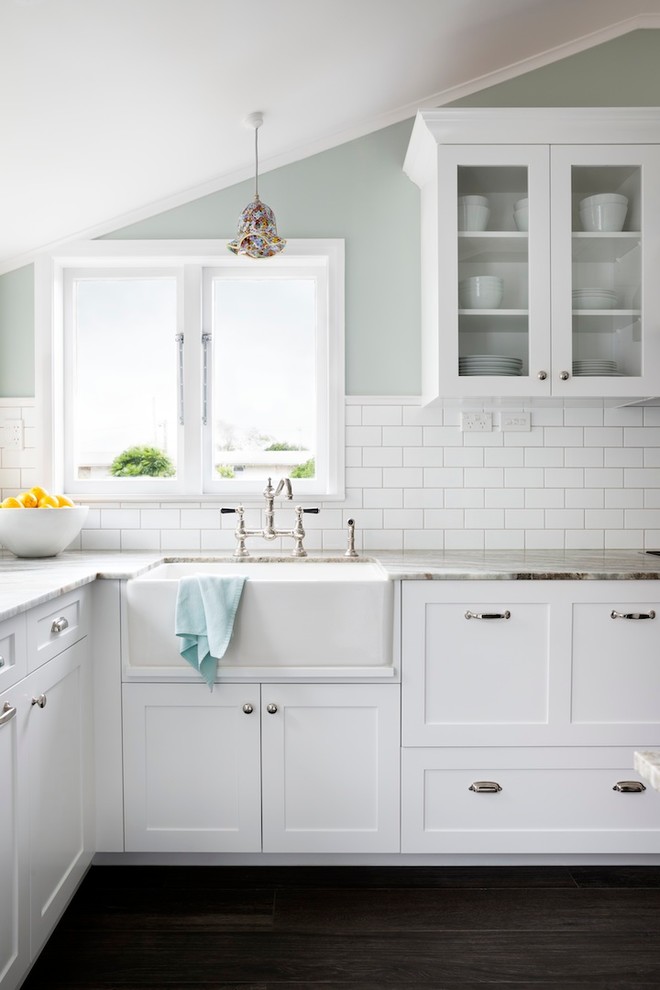 Inspiration for a mid-sized timeless u-shaped porcelain tile kitchen remodel in Auckland with a farmhouse sink, recessed-panel cabinets, white cabinets, granite countertops, white backsplash, stainless steel appliances and subway tile backsplash