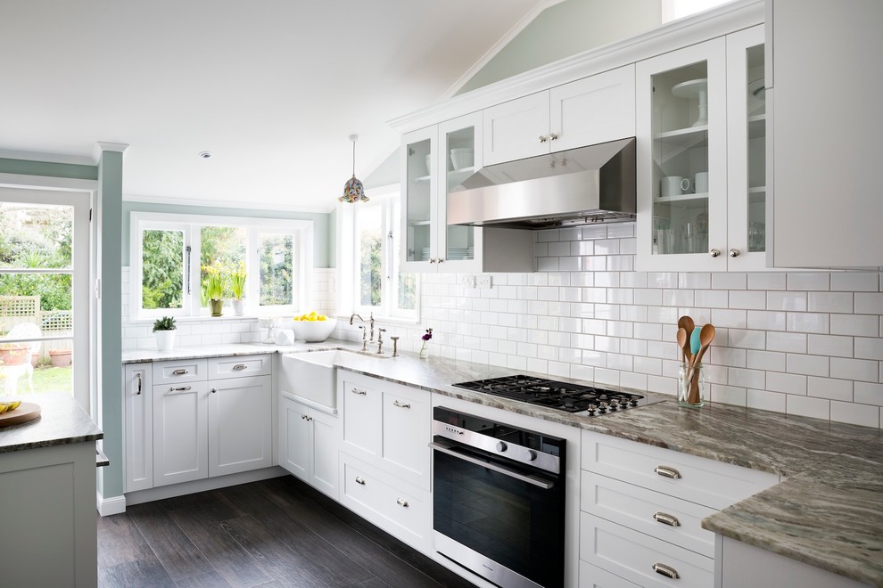 Inspiration for a mid-sized timeless u-shaped porcelain tile eat-in kitchen remodel in Auckland with a farmhouse sink, recessed-panel cabinets, white cabinets, granite countertops, white backsplash, ceramic backsplash, stainless steel appliances and a peninsula