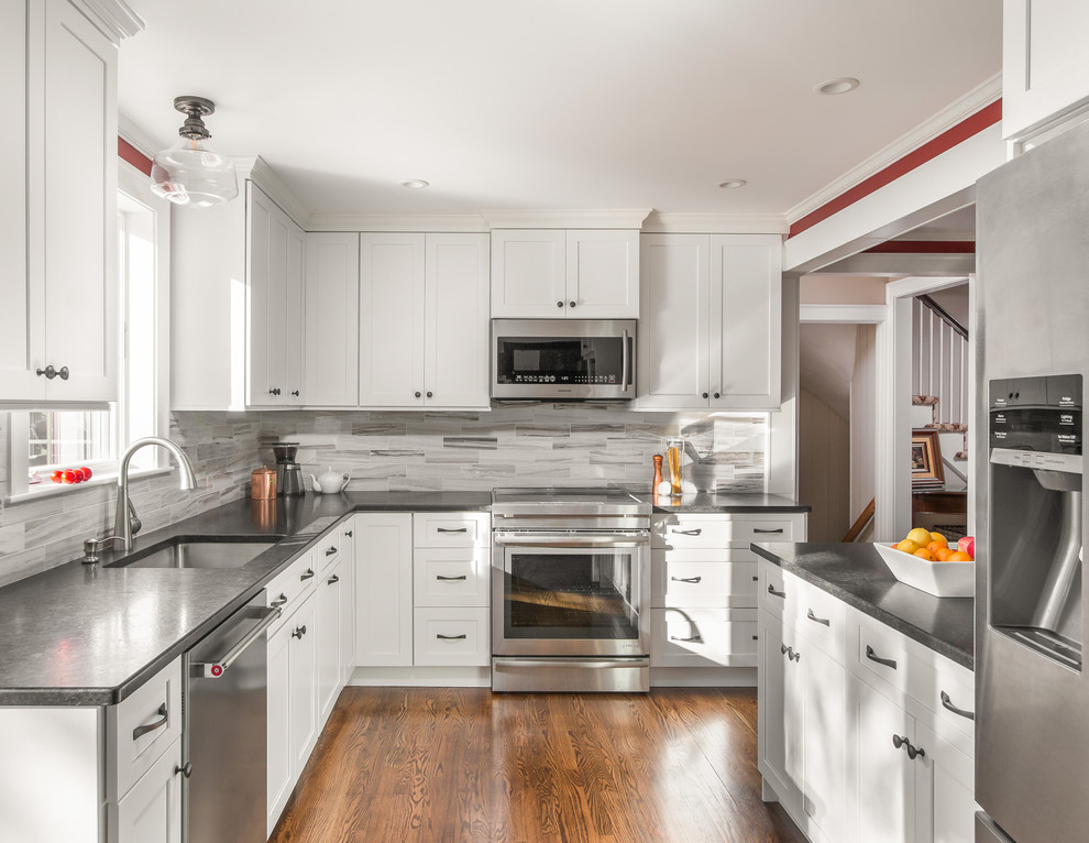 Photo of a traditional u-shaped enclosed kitchen in Boston with a single-bowl sink, shaker cabinets, white cabinets, grey splashback, metro tiled splashback, stainless steel appliances, medium hardwood flooring and brown floors.