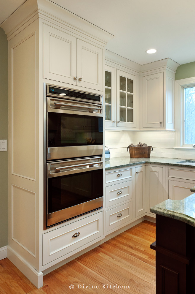 Inspiration for a large timeless l-shaped medium tone wood floor eat-in kitchen remodel in Boston with an undermount sink, beaded inset cabinets, white cabinets, granite countertops, white backsplash, ceramic backsplash, stainless steel appliances and an island
