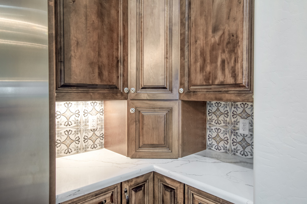 Inspiration for a large traditional l-shaped kitchen/diner in Phoenix with a submerged sink, raised-panel cabinets, medium wood cabinets, beige splashback, ceramic splashback, stainless steel appliances, an island, grey floors and white worktops.